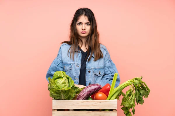 Young farmer woman holding a basket full of fresh vegetables sad