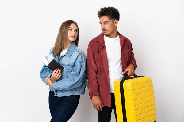 旅行者のカップルは笑顔で肩越しに見て青い背景に隔離されたスーツケースを持っています — ストック写真
