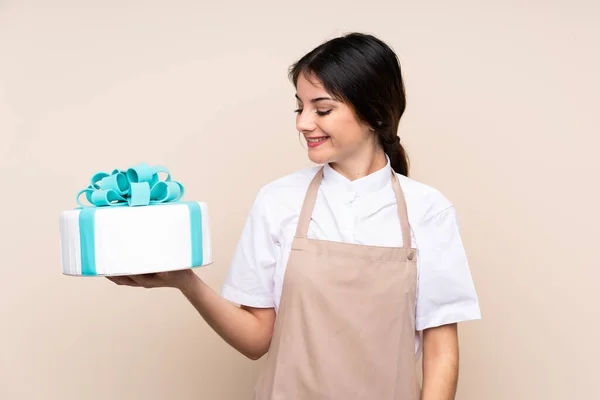 Pastry chef woman holding a big cake over isolated background with happy expression