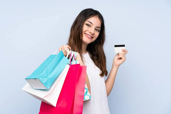 一个年轻的黑发女人 带着购物袋和信用卡 站在孤立的蓝色背景上 — 图库照片