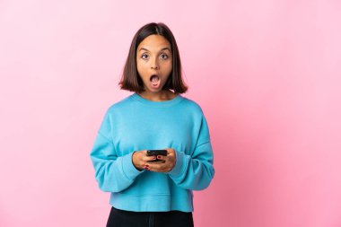 Pembe arka planda izole edilmiş genç Latin kadın şaşırdı ve bir mesaj gönderiyor.