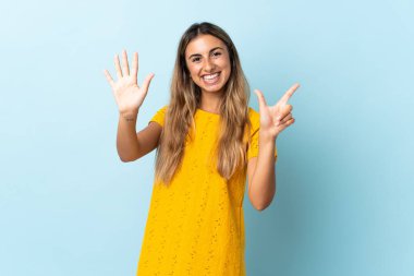 İzole edilmiş mavi arka planda genç İspanyol kadın parmaklarıyla yediyi sayıyor