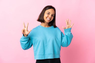 Pembe arka planda izole edilmiş genç Latin kadın parmaklarıyla sekiz sayıyor.