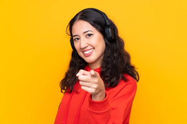 Kırmızı kazaklı melez bir kadın müzik dinliyor ve ön tarafı işaret ediyor.