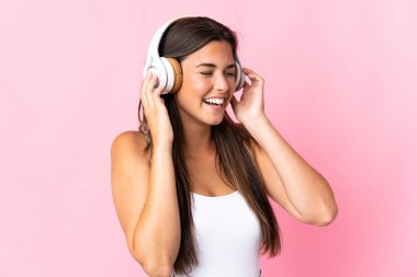 Pembe arka planda izole edilmiş genç Brezilyalı kız müzik dinliyor ve şarkı söylüyor.