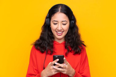 Kırmızı kazaklı melez bir kadın müzik dinliyor ve cep telefonu arıyor.