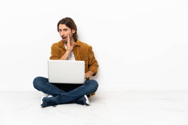 Dizüstü bilgisayarı olan genç bir adam yerde oturmuş bir şeyler fısıldıyor.