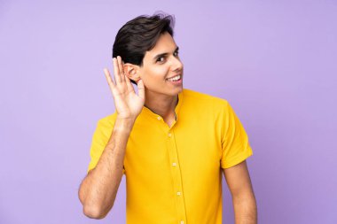 İzole edilmiş mor arka planda bir adam elini kulağına koyarak bir şeyler dinliyor.