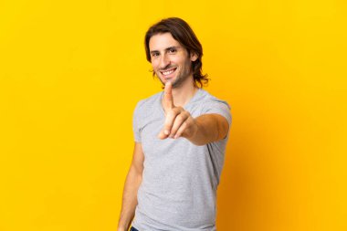 Sarı arka planda izole edilmiş genç yakışıklı adam parmağını kaldırıyor ve gösteriyor.