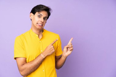 İzole edilmiş mor arka planda korkmuş ve yüzünü gösteren bir adam var.