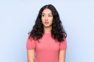 Melez ırktan bir kadın, izole edilmiş mavi arka planda süveter giyiyor ve yan tarafa bakıyor.