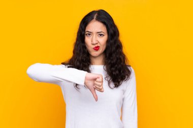 Karma ırk kadını, izole edilmiş sarı arka planda, baş parmak aşağı işareti gösteriyor.