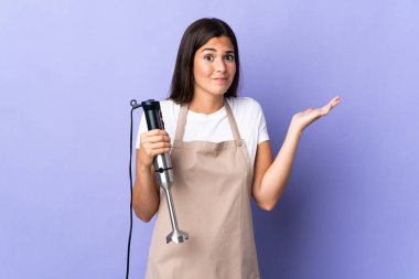 Mor arka planda izole edilmiş el blenderi kullanan Brezilyalı kadın ellerini kaldırırken şüphe duyuyor