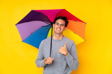 Sarı arka planda şemsiyesi olan bir adam baş parmak hareketi yapıyor.