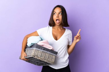 Mor arka planda izole edilmiş çamaşır sepetini tutan genç latin kadın bir fikrin parmağı yukarı kaldırdığını düşünüyor.