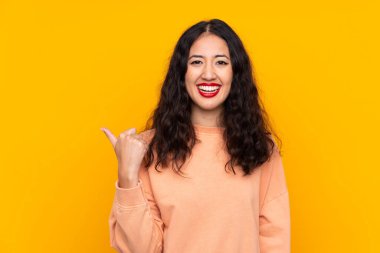 İspanyol Çinli kadın izole edilmiş sarı arka planda bir ürün sunmak için kenarı işaret ediyor.