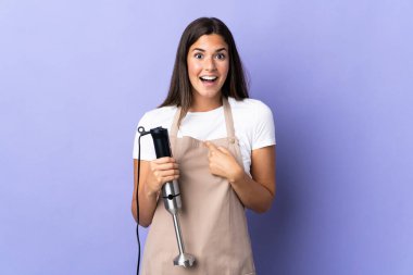 Mor arka planda izole edilmiş el blenderi kullanan Brezilyalı bir kadın.