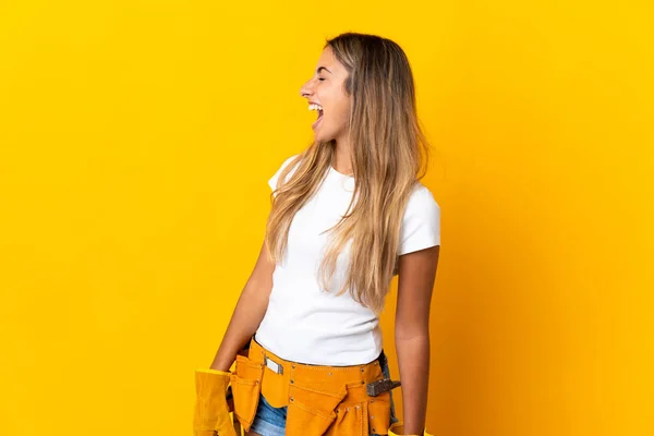 Young hispanic electrician woman over isolated yellow wall laughing in lateral position