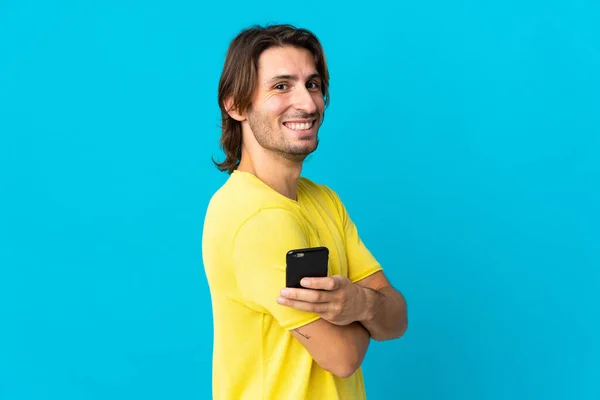 Young Handsome Man Isolated Blue Background Holding Mobile Phone Arms — Stock Photo, Image