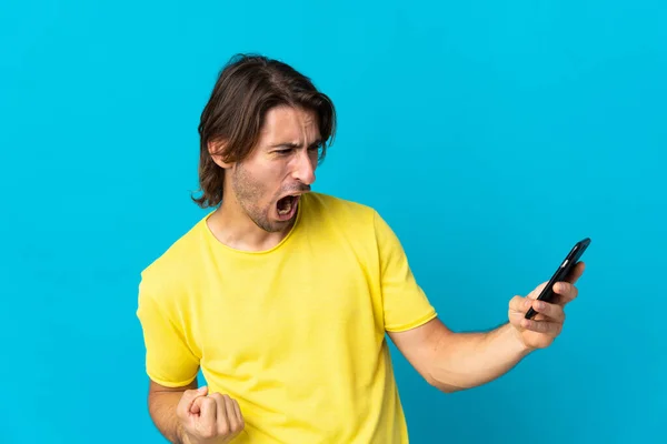 Mladý Pohledný Muž Izolovaný Modrém Pozadí Pomocí Mobilního Telefonu Dělá — Stock fotografie