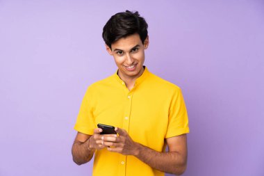 İzole edilmiş mor arkaplan üzerinde adam cep telefonuyla bir mesaj gönderiyor