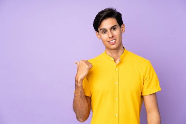 İzole edilmiş mor arka planda bir adam bir ürünü sunmak için kenarı işaret ediyor.