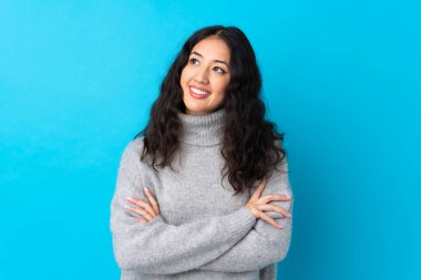 İspanyol Çinli kadın mavi arka planda, gülümserken yukarı bakıyor.