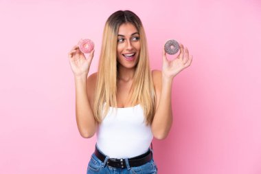 Genç Uruguaylı kadın pembe arka planda donut tutuyor ve şaşırıyor.