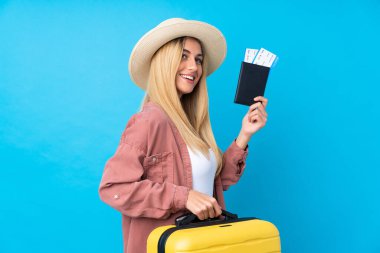 Genç Uruguaylı kadın izole edilmiş mavi arka planda, bavul ve pasaportla tatilde.