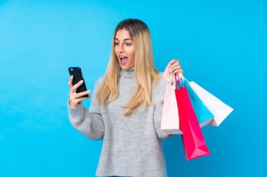Genç Uruguaylı kadın mavi arka planda, elinde alışveriş torbalarıyla bir arkadaşına cep telefonuyla bir mesaj yazıyor.