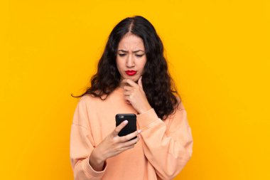 İspanyol Çinli kadın izole edilmiş sarı arka plan düşünüyor ve bir mesaj gönderiyor.