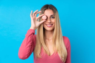 Genç Uruguaylı kadın izole edilmiş mavi arka planda elinde renkli Fransız kurabiyeleri tutuyor.