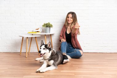 Köpeği evde yerde oturan genç bir kız. Eli ile gelmesi için davet ediyor. Gelmene sevindim.