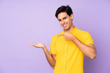 İzole edilmiş mor arkaplan üzerindeki adam bir reklam eklemek için avucunun içinde hayali bir alan tutuyor