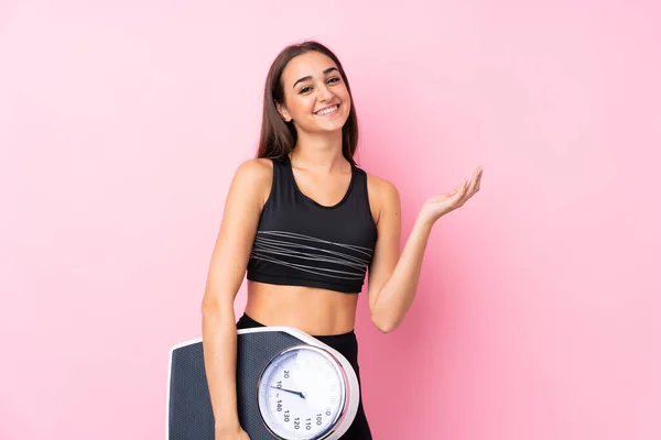 Pretty young girl with weighing machine over isolated pink background with weighing machine