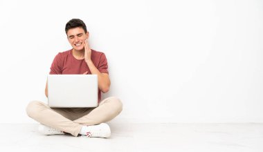 Flor 'da dizüstü bilgisayarı ve diş ağrısı olan genç bir adam oturuyor.