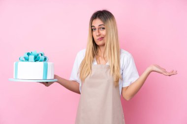 Gencecik Uruguaylı pastacı kadın pembe arka plan üzerinde büyük bir pastayla omuzlarını kaldırırken şüphe uyandırıyor.