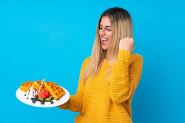 İzole edilmiş arka planda waffle tutan genç bir kadın zaferi kutluyor.