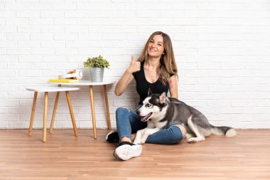 Genç ve güzel bir kadın, iri köpeğiyle baş parmaklarını kaldırarak yerde oturuyor. Çünkü iyi bir şey oldu.