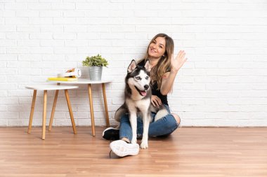 İri köpeğiyle yerde oturan genç ve güzel bir kadın mutlu bir ifadeyle selamlıyor.