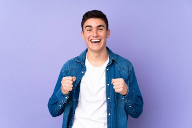 Mor arka planda izole edilmiş beyaz, yakışıklı genç bir adam galibiyeti kutluyor.