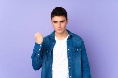 Genç, beyaz, yakışıklı bir adam. Mor arka planda, öfkeli bir jestle izole edilmiş.