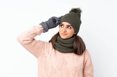 Kışlık şapkalı genç kız izole beyaz arka planda kuşkuları ve kafa karıştırıcı bir yüz ifadesi var.