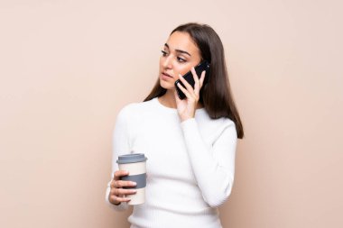 Arka planda izole edilmiş genç bir kadın elinde kahve ve bir cep telefonu tutuyor.