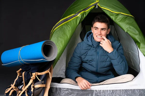 Teenager caucasian man inside a camping green tent isolated on black background nervous and scared