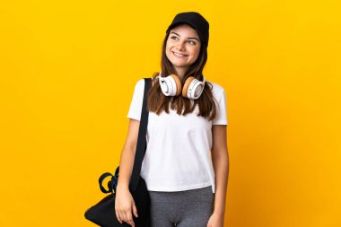 Spor çantalı genç bayan sarı arka planda izole edilmiş bir şekilde yukarı bakarken bir fikir düşünüyor.