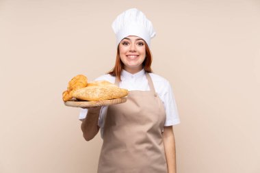 Şef üniformalı kızıl saçlı genç kız. Kadın fırıncı elinde birkaç ekmekle bir masa tutuyor. Şaşırmış ve şok olmuş yüz ifadesi var.