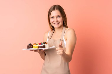 Ukraynalı aşçı pembe arka planda izole edilmiş bir kek tutuyor.