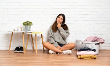 Genç bir kadın çamaşır sepetiyle yerde oturuyor. Şüpheleri var.