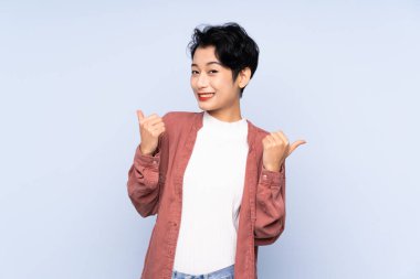 Asyalı genç bir kız soyutlanmış mavi bir geçmişi var. Başparmakları havada ve gülümsüyor.